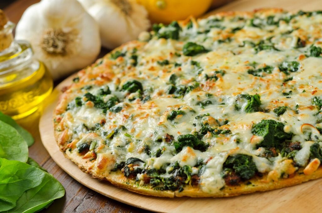 A freshly baked thin crust spinach pizza with garlic, lemons, and olive oil.